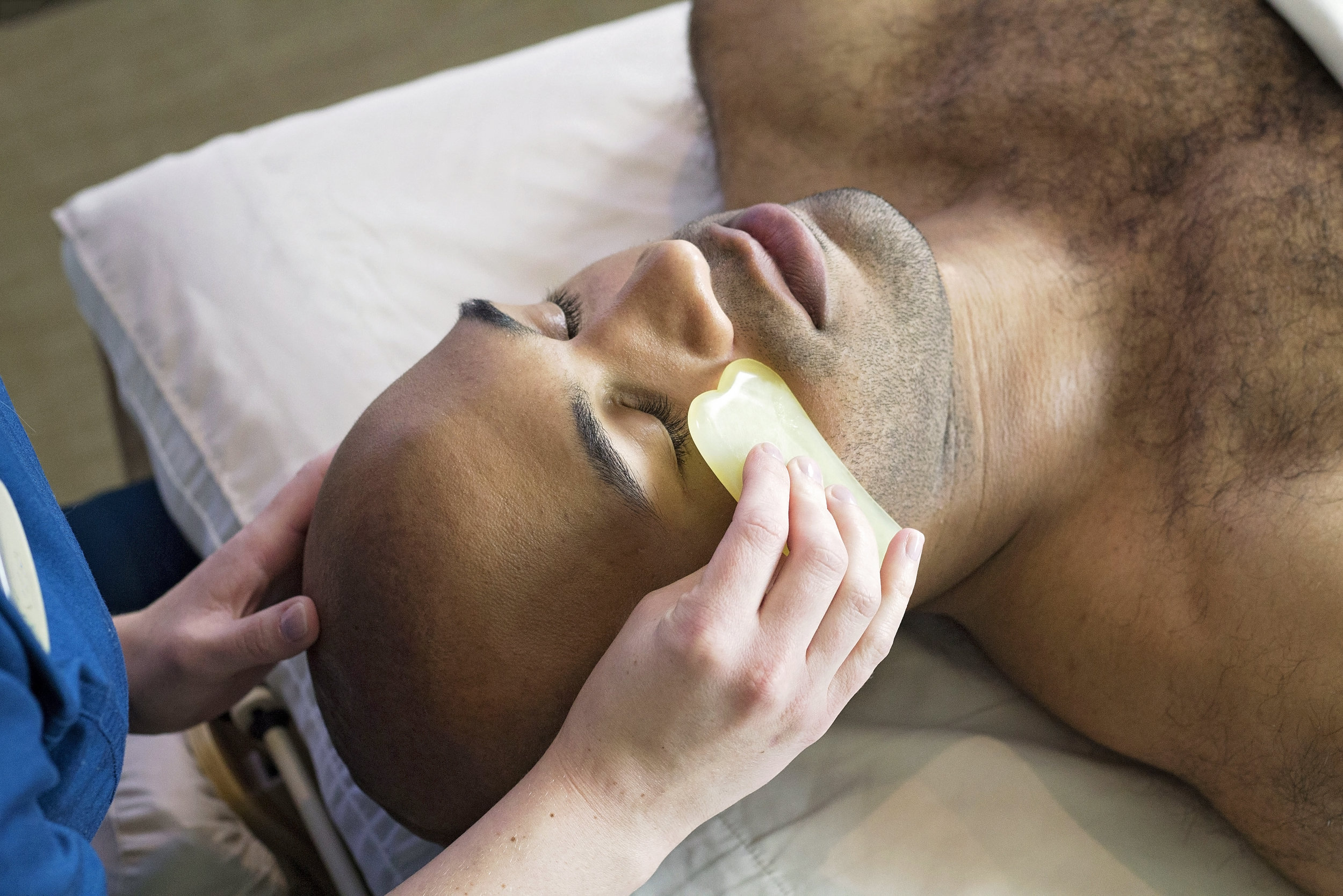 Multiracial man receiving a gua sha massage using a speciality jade stone