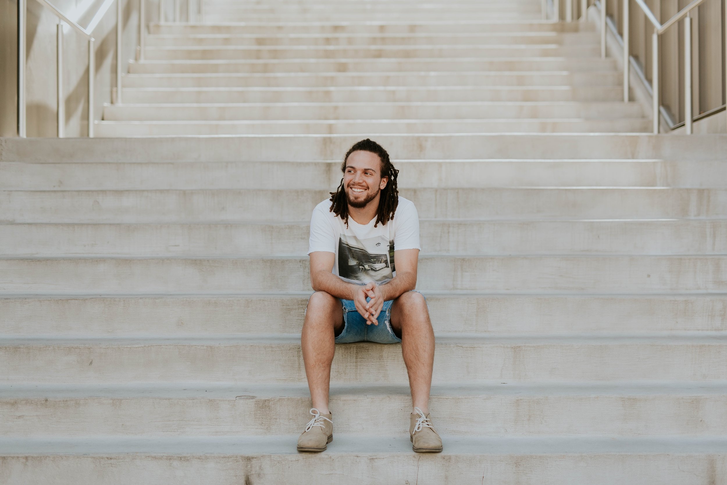 Man with dreadlocks sitting on white stairs while smiling