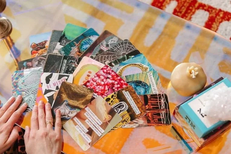 Handmade collaged Intuition Cards are spread on a table with a pomegranate candle and a deck of oracle cards.