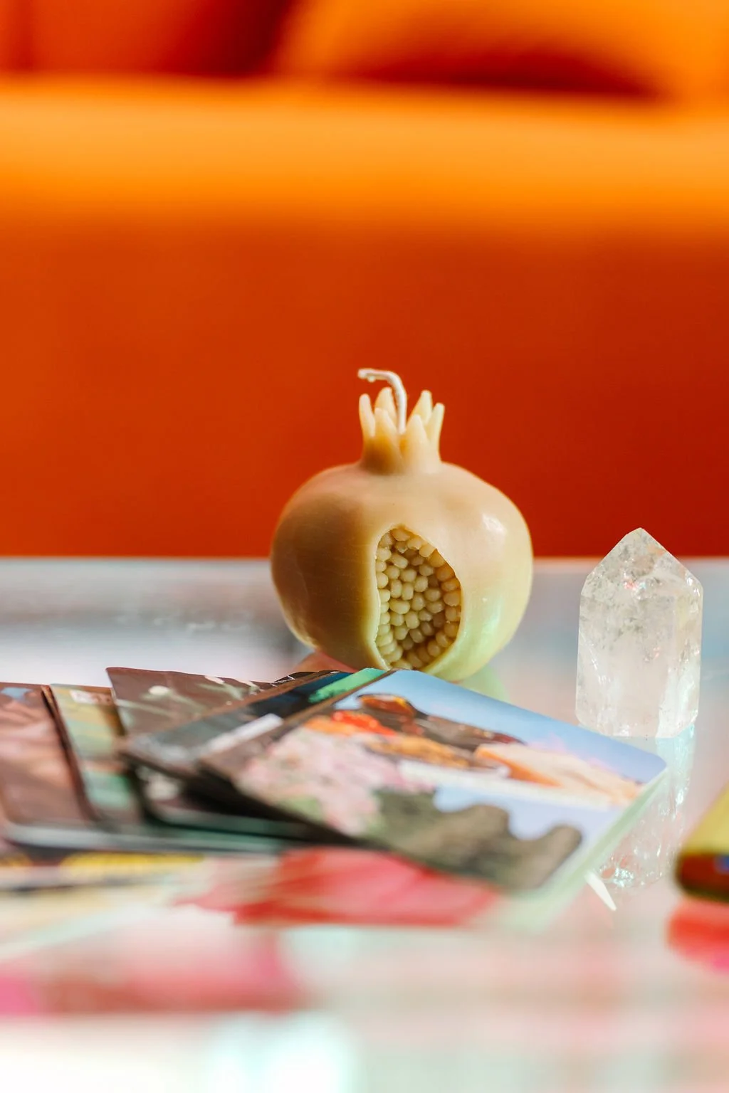 A photo of a table scape with a pomegranate candle, handmade oracle cards, and clear quartz crystal