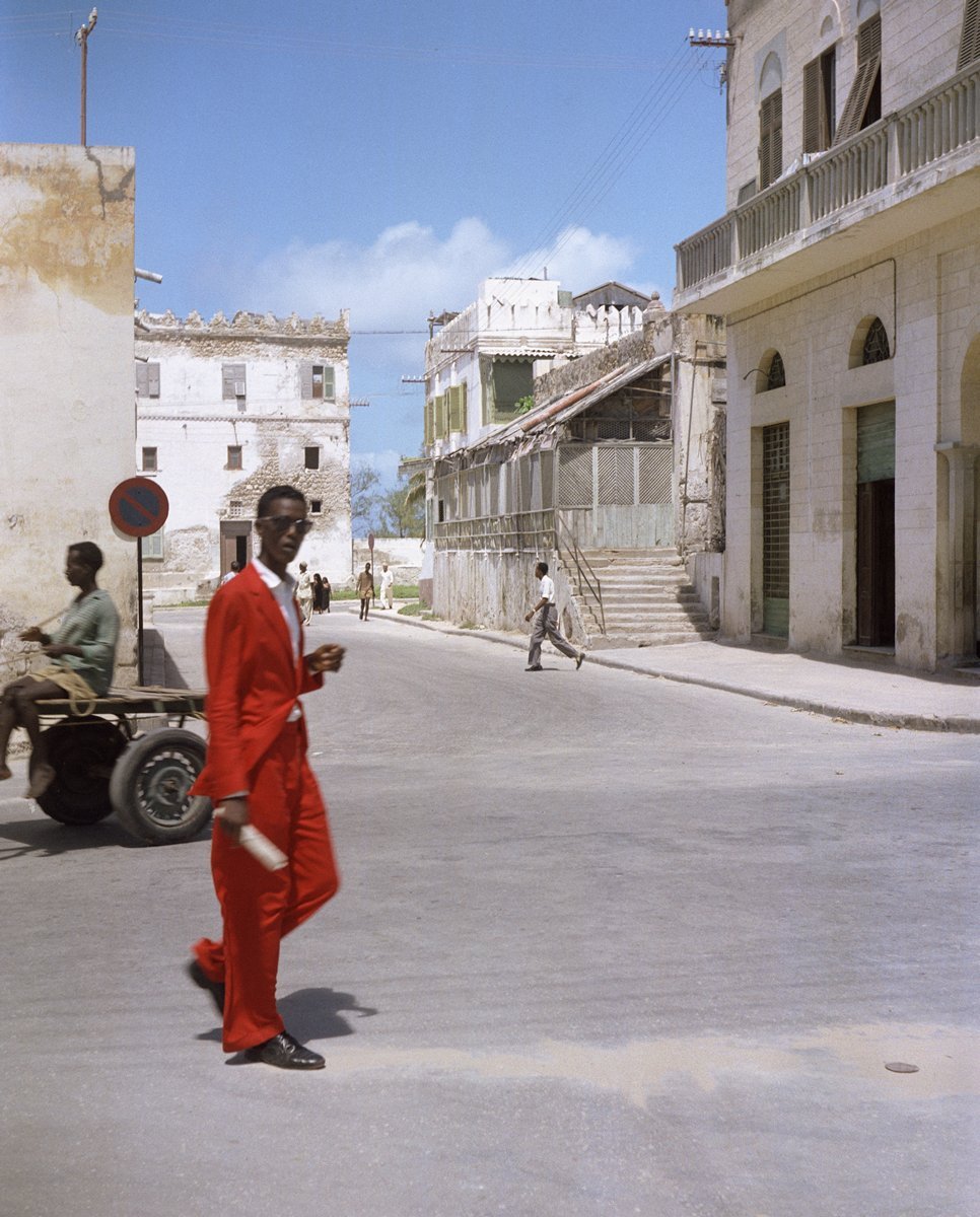  Todd Webb (United States, 1905-2000),  Untitled (44UN-8001-496), Somaliland (Somalia)  [Man in red suit walking in Mogadishu], 1958, archival pigment print, 16 x 20 inches (image), 18 x 22 inches (sheet). © Todd Webb Archive 