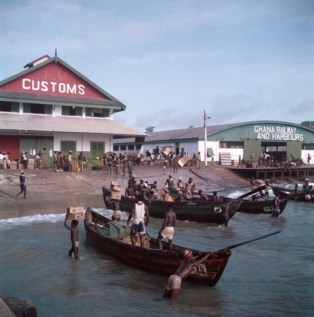  Todd Webb (United States, 1905-2000),  Untitled (44UN-7997-226), Ghana  [Unloading cargo with Customs House and Ghana Railway and Harbours in the background, Accra], 1958, archival pigment print, 14 x 14 inches (image), 16 x 16 inches (sheet). © Tod