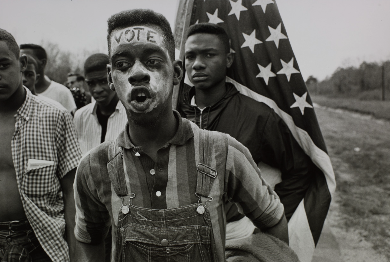   Bruce Davidson  United States, born 1933   Time of Change (Young Man with "Vote" painted on his forehead walking in the Selma March, Alabama) , 1965 gelatin silver print, 16 x 20 inches Promised Gift from the Judy Glickman Lauder Collection, 8.2021