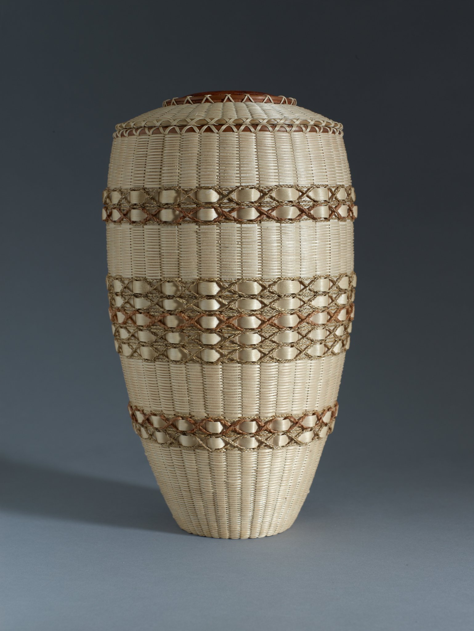  Jeremy Frey (Passamaquoddy, born 1978),  Covered Vase , 2016, ash, cedar bark, cherry wood, sweetgrass, and spruce root, 14 3/4 x 7 x 7 inches. Portland Museum of Art, Maine. Gift of Barbara M. Goodbody, 2021.19.6a,b. © Jeremy Frey. Image courtesy L