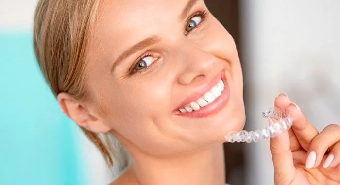 Mujer sonriendo y sosteniendo un aparato de alineación dental transparente.