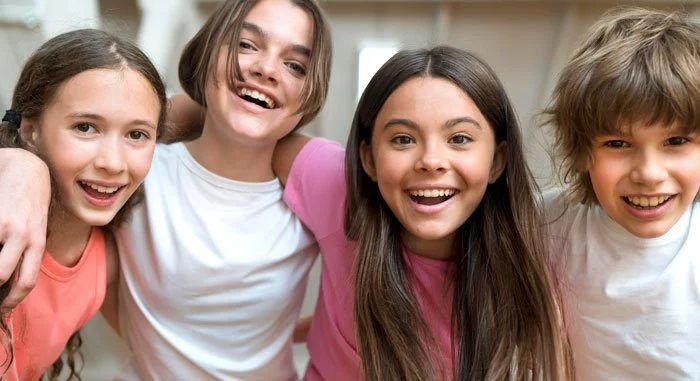 Cuatro niños sonriendo y posando juntos en una habitación bien iluminada.