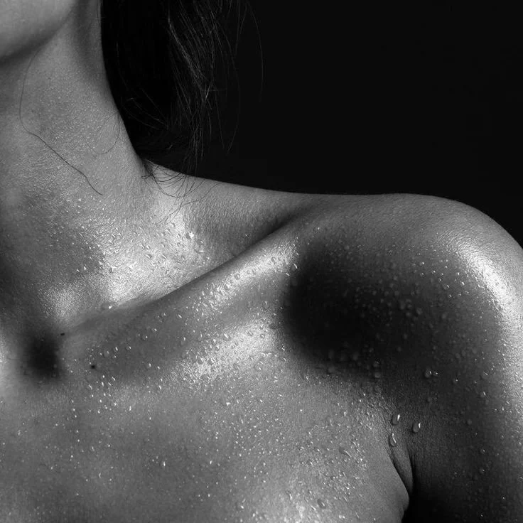 Close-up of a wet woman's shoulder and collarbone area, with water droplets on her skin, in black and white.