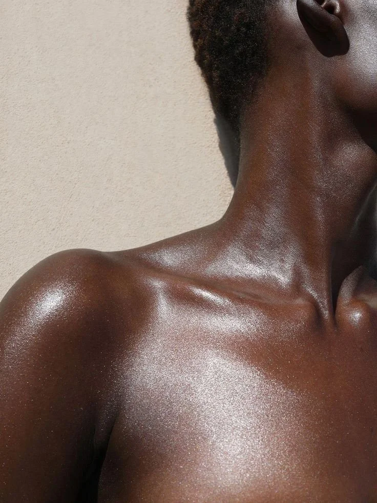 Close-up of a person's shoulder and neck with smooth, shiny skin, and a portion of their face and hair visible.