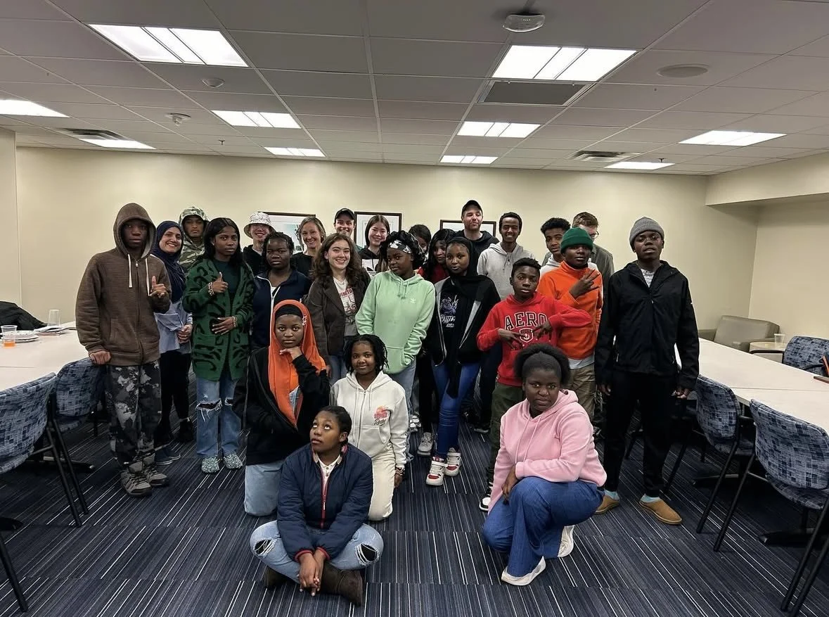 Group of young people and children posing in a conference room with tables and chairs.