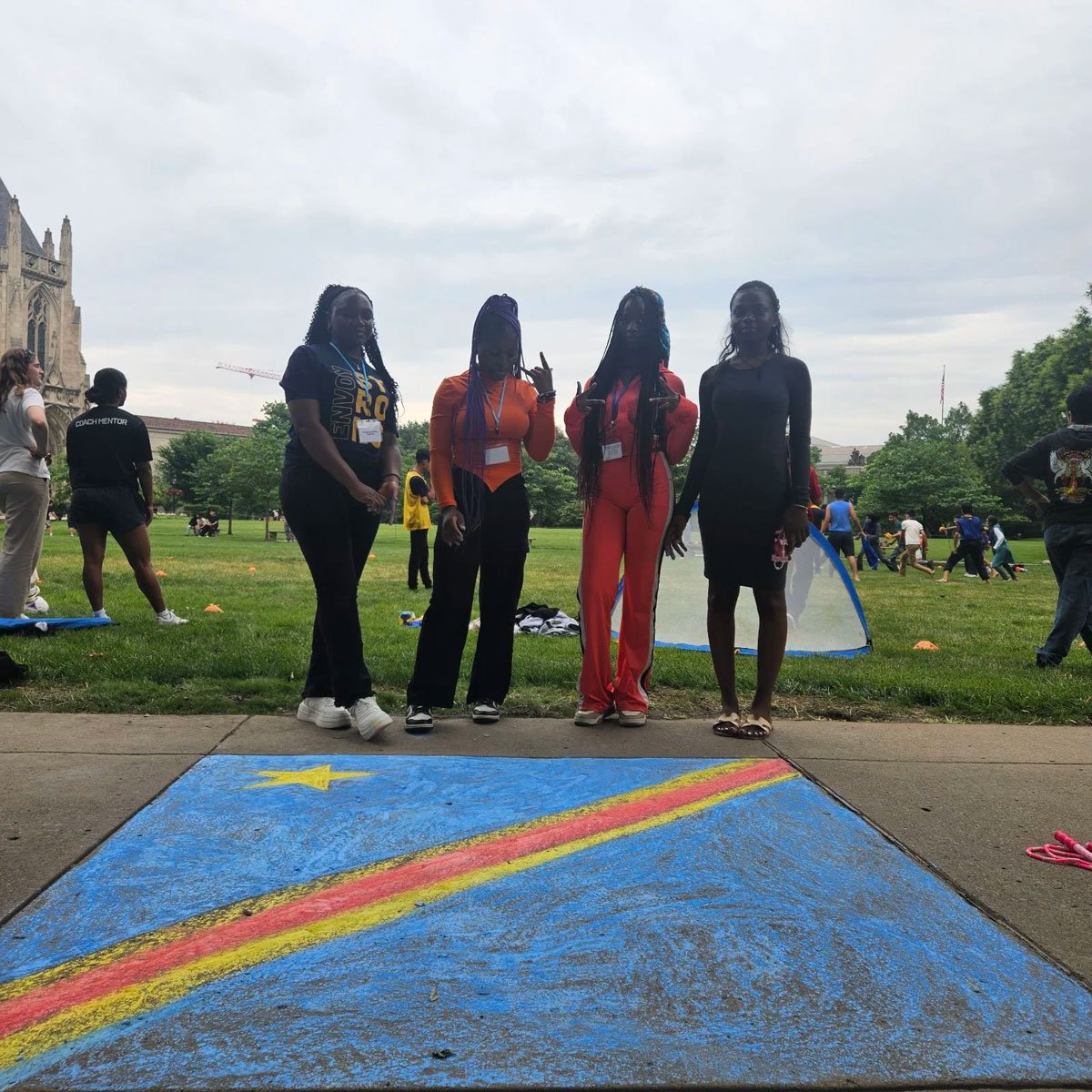Four students standing in front of chalk drawing of a rainbow in blue sky