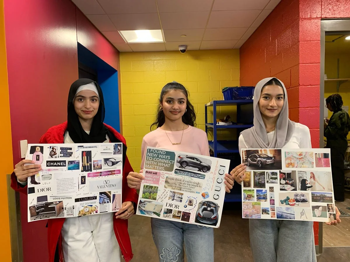 Three young women standing indoors, each holding a collage poster with images of luxury brands, cars, and fashion items.
