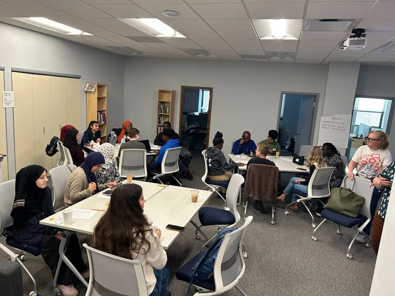 A diverse group of people participating in a meeting or workshop in a conference room with bookshelves and a whiteboard.
