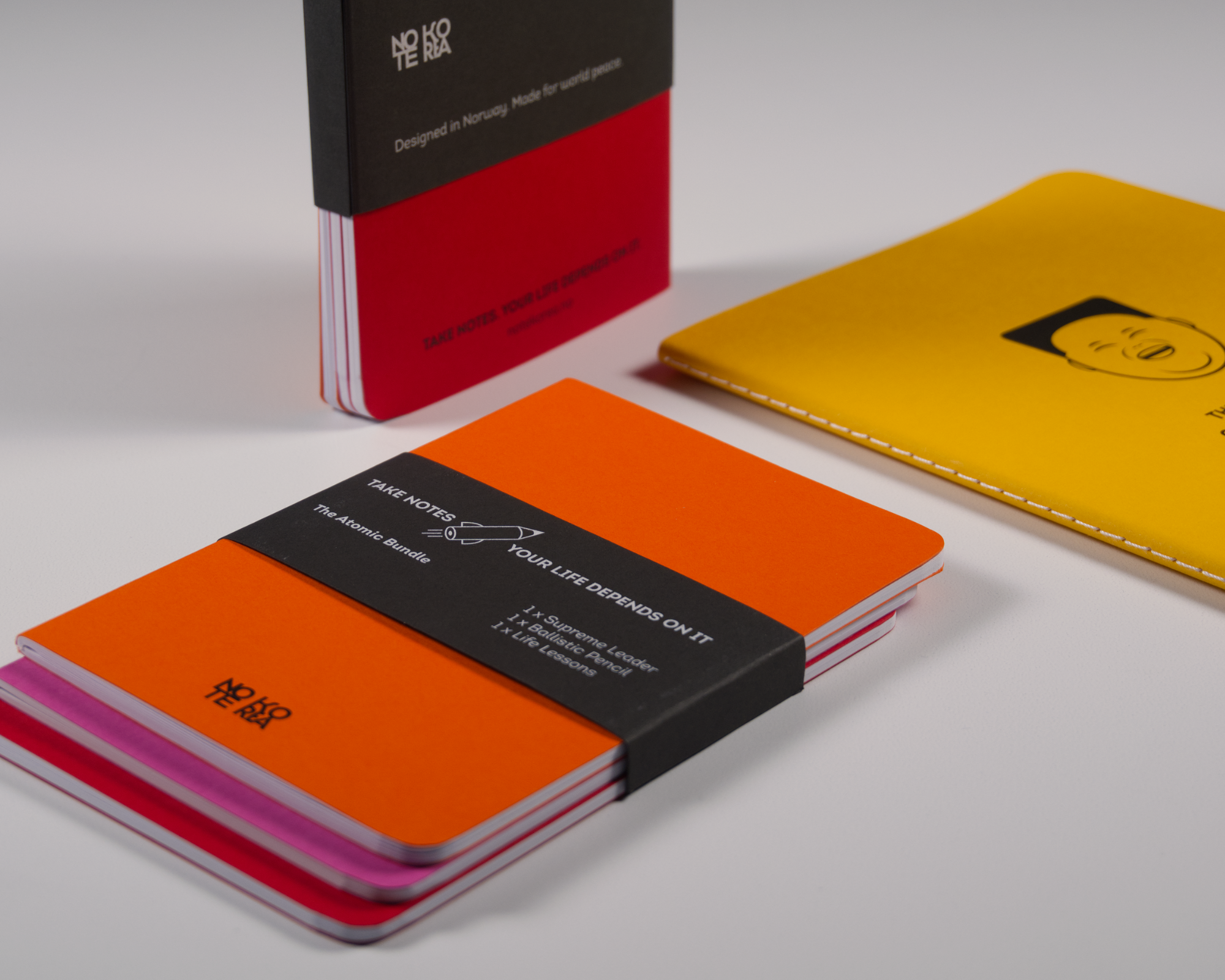 Close-up of several colorful notebooks or planners with covers in black, red, orange, yellow, and pink, placed on a white surface.
