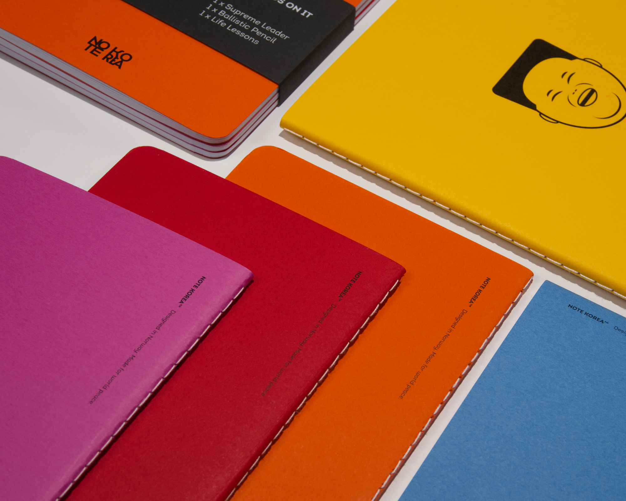 Close-up of colorful notebooks, including pink, red, orange, yellow, and blue, arranged on a white surface.