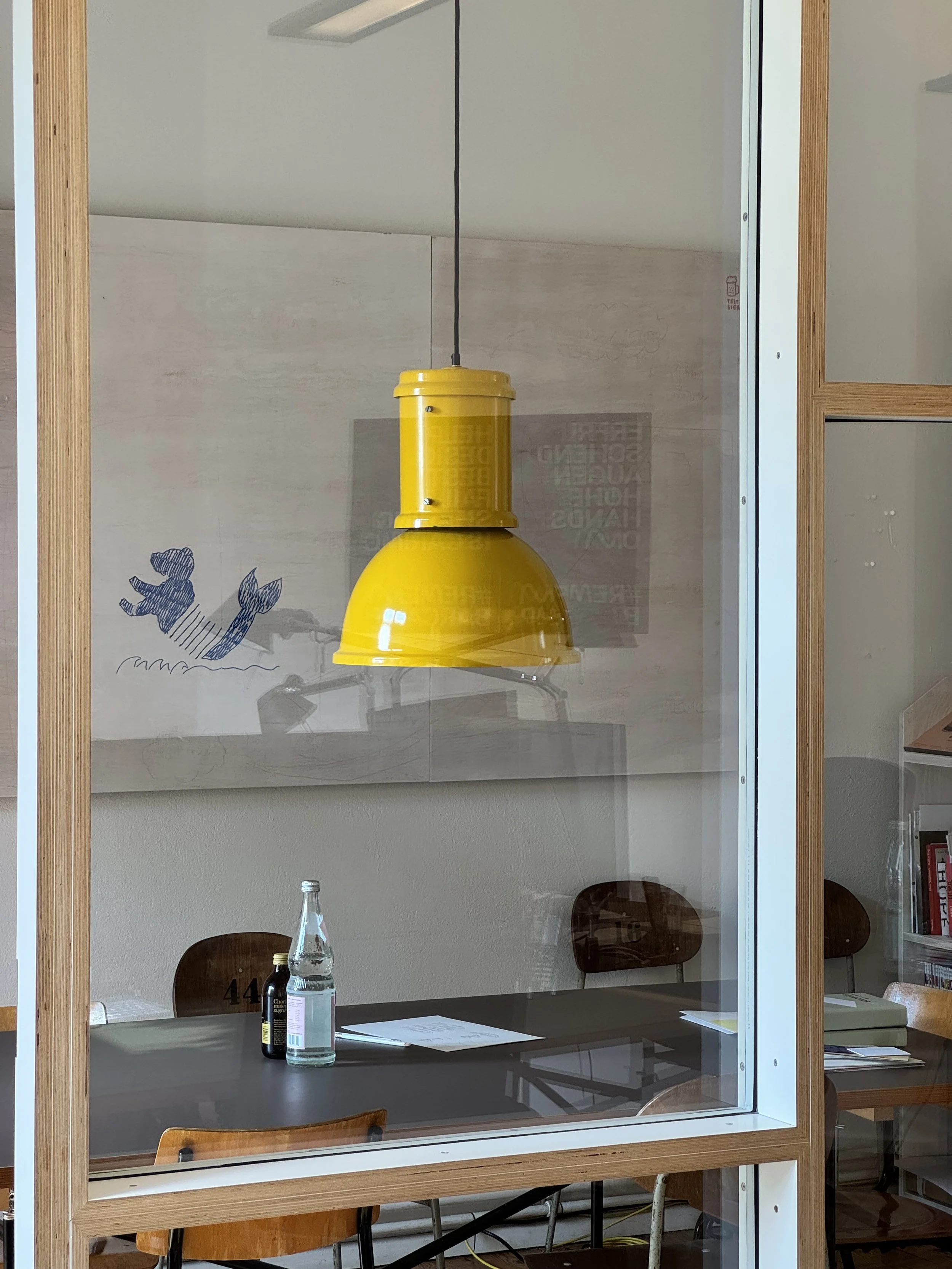 Blick durch Glastrennwand mit Arbeitstisch und gelber Deckenleuchte