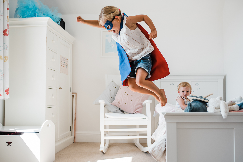 girl in superhero costume jumping off bed