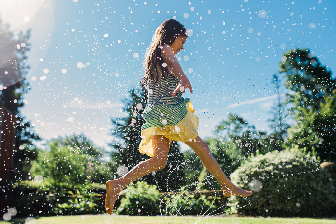 girl jumping through sprinkler at grandparents home