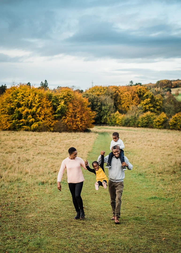 Family of four laughing while walking across a grassy field surrounded by autumnal trees