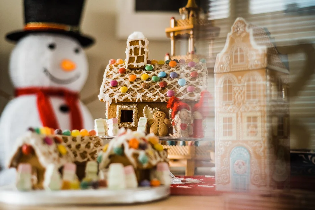 Photo of Gingerbread houses big and small with marshmallows, snowman in the background and cookie tin in the foreground
