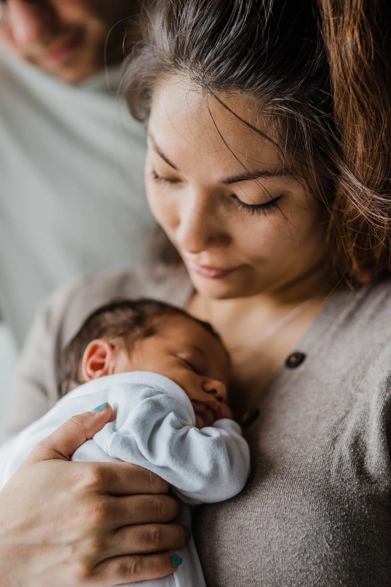 New mother cuddling her newborn baby by the window at home, photographed naturally and unposed