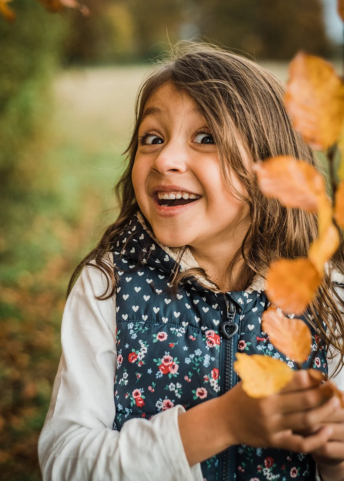 Girl smiling while holding a branch of leaves during an autumn photoshoot