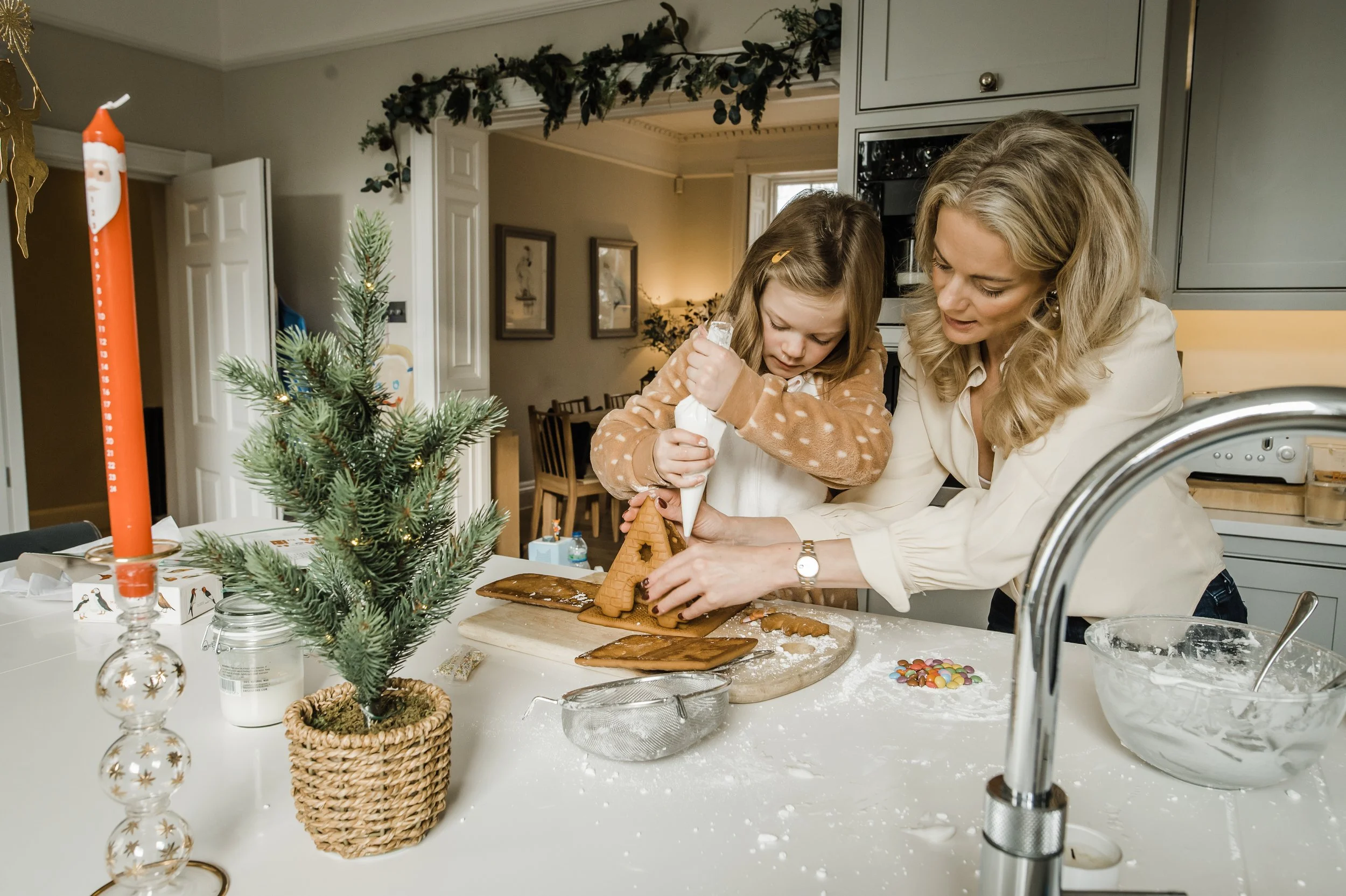 Photo of a Mother and daughter icing a gingerbread house at Christmas in the kitchen