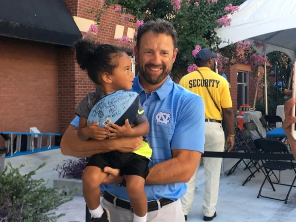 Head coach Larry Fedora holds a young UNC fan at the "Meet the Heels" event on Saturday.
