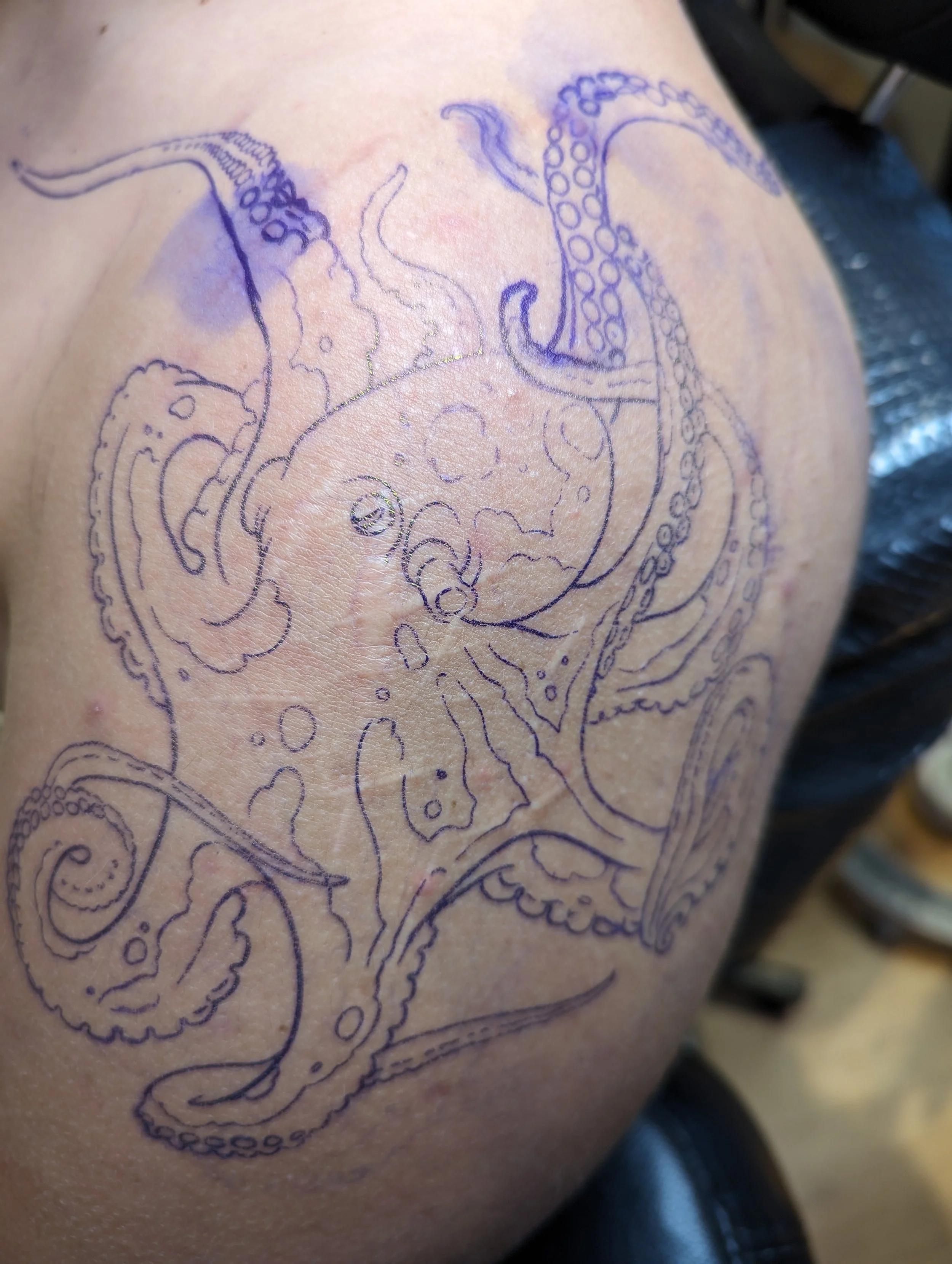 Outline sketch of an octopus drawn on someone's shoulder with a marker.
