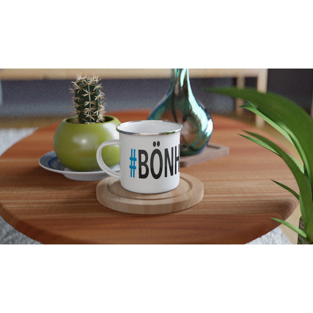 The picture shows a left side view of the 12oz white enamel mug "#BÖNHAMN Höga Kusten" from the series HIKING #TAGMUG™ on a contemporary kitchen table