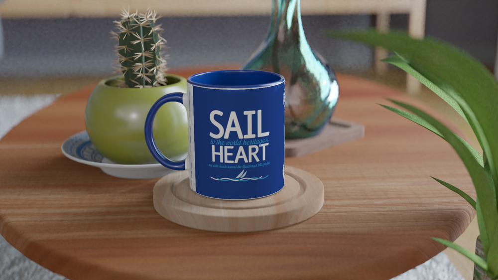 The picture shows a left side view of the 11oz ceramic mug "SAIL TO THE WORLD HERITAGE HEART” from the series HIGH COAST SAILOR #TAGMUG™ with blue color inside on a contemporary kitchen table