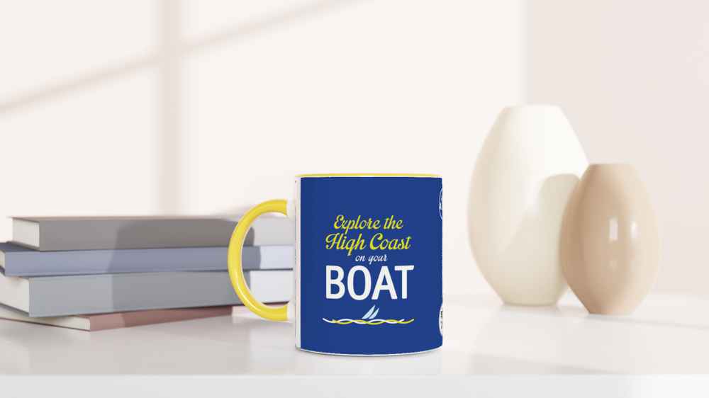 The picture shows a left side view of the 11oz ceramic mug "EXPLORE THE HIGH COAST" from the series HIGH COAST SAILOR #TAGMUG™ with yellow color inside on a desktop