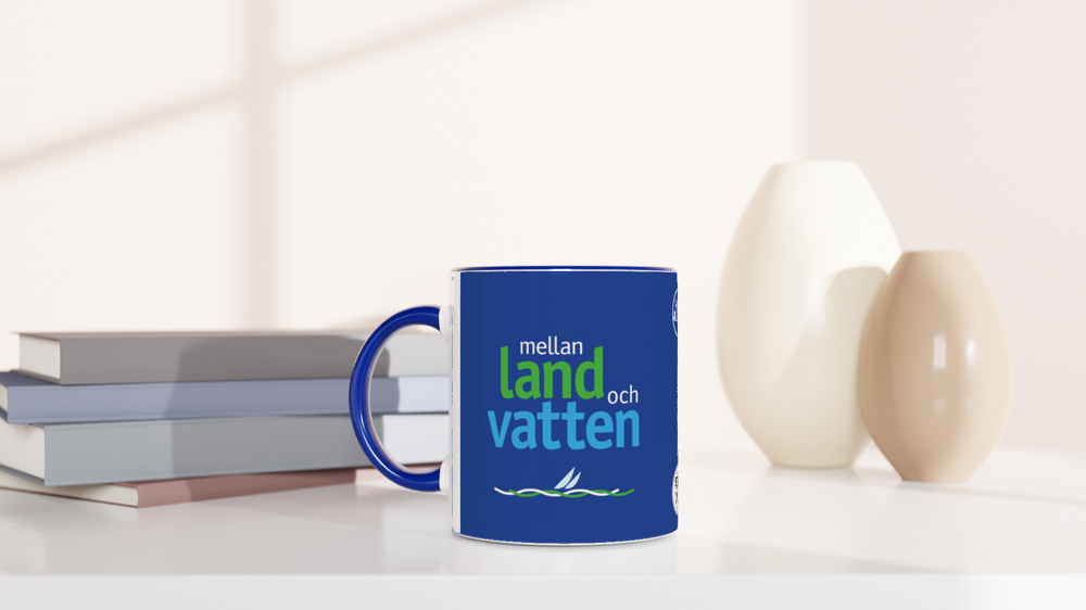 The picture shows a left side view of the 11oz ceramic mug "MELLAN LAND OCH VATTEN" from the series HIGH COAST SAILOR #TAGMUG™ with blue color inside on a desktop