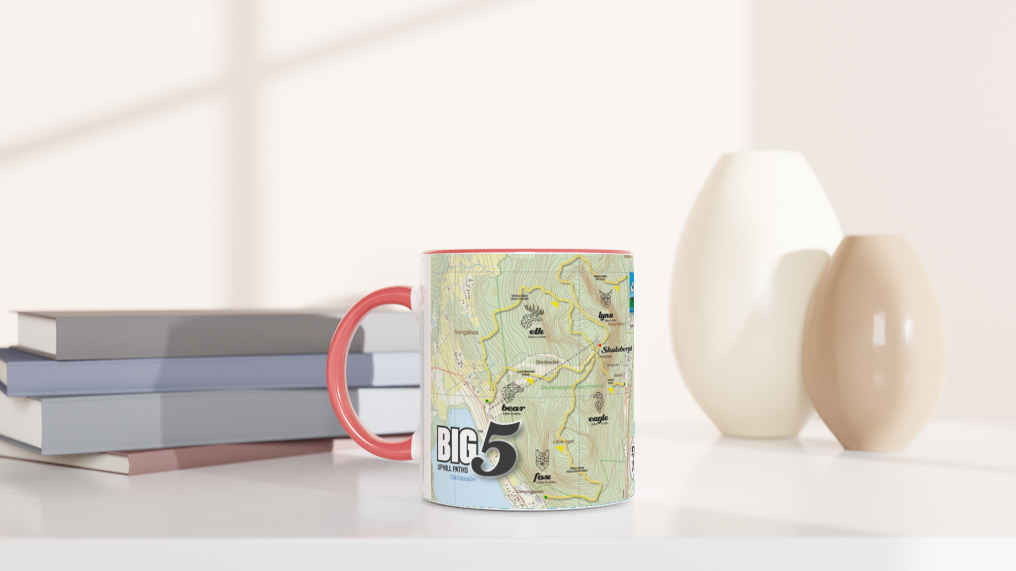 The picture shows a left side view of the 11oz ceramic mug "SKULEBERGET FOX PATH" from the series “SKULE BIG5" #TAGMUG™ with pink color inside on a desktop