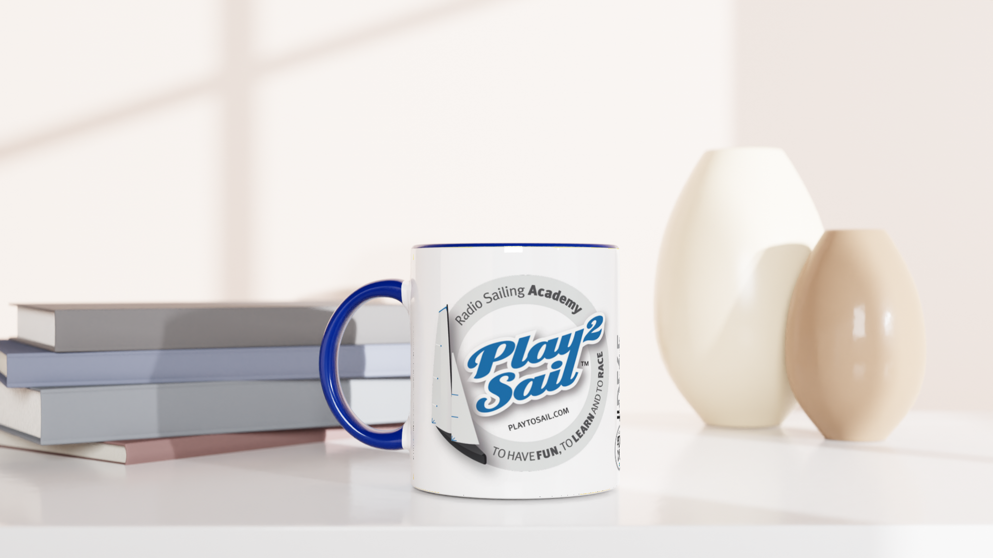 The picture shows a left side view of the 11oz ceramic mug "RADIO SAILING ACADEMY" from the series PLAY2SAIL #TAGMUG™ with blue color inside on a desktop