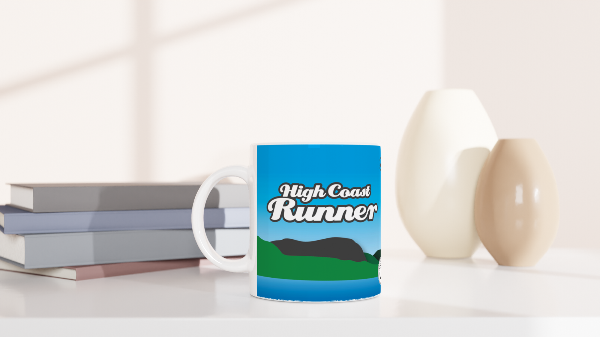 The picture shows a left side view of the 11oz ceramic mug "RUN UP AND DOWN THE HILLS” from the series HIGH COAST RUNNER #TAGMUG™ on a desktop