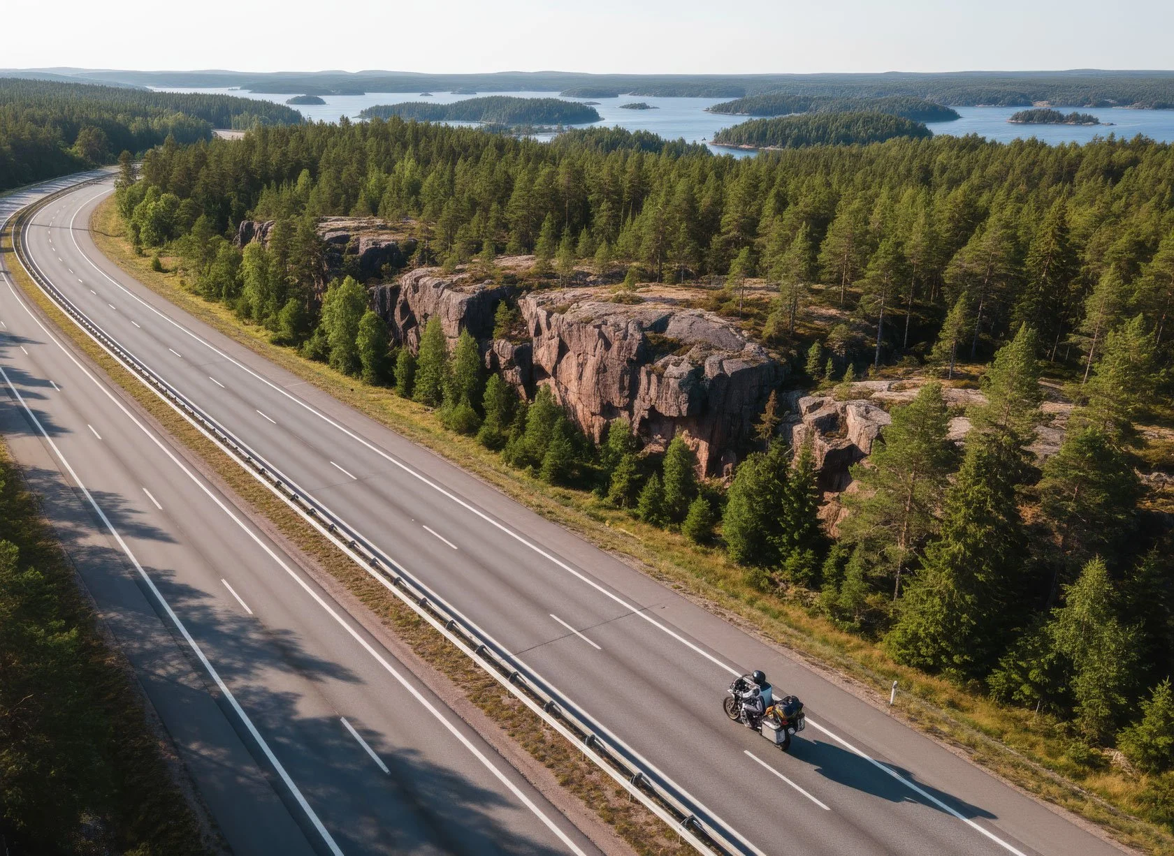 Long-distance motorcycle rider with touring panniers heading north on Sweden's E4 highway through Höga Kusten (High Coast), red granite cliffs and blue fjord visible, safe overnight stopover at Docksta Havet