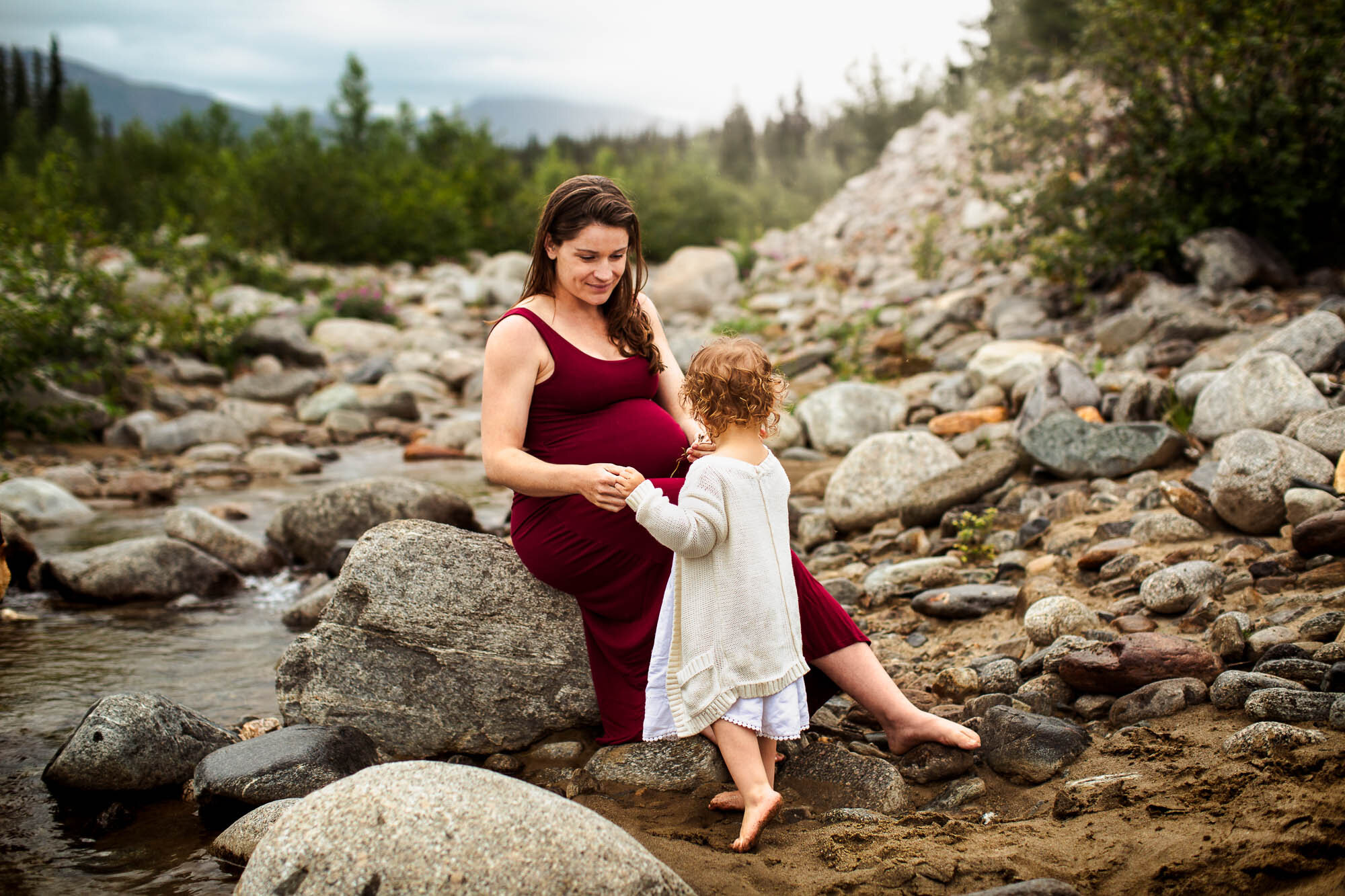 Alaska Family Photographer, pregnant mother sitting on a rock holding hand with young daughter