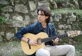 Italian man playing the guitar, wearing a denim jacket.
