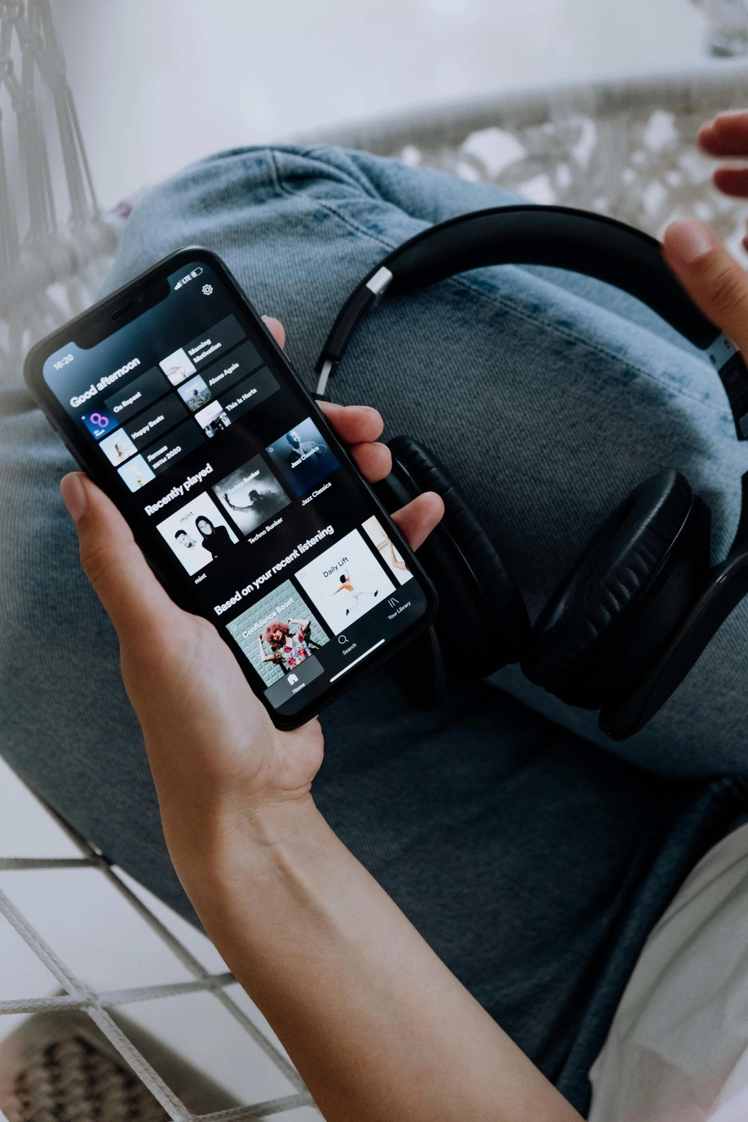 Music listener holding a phone showing a music streaming app beside headphones