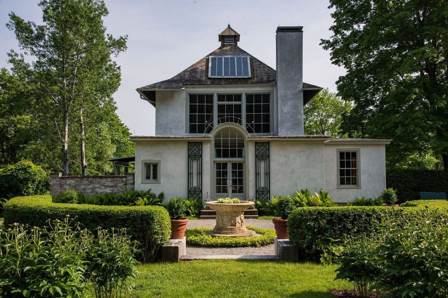 Counting the days till spring...⁠
⁠
⁠
. . .⁠
⁠
{image: A stucco building with large windows and skylight, sits amid large green trees, in a lush, green garden with a classical inspired fountain centered before the building&rsquo;s French doors. The S