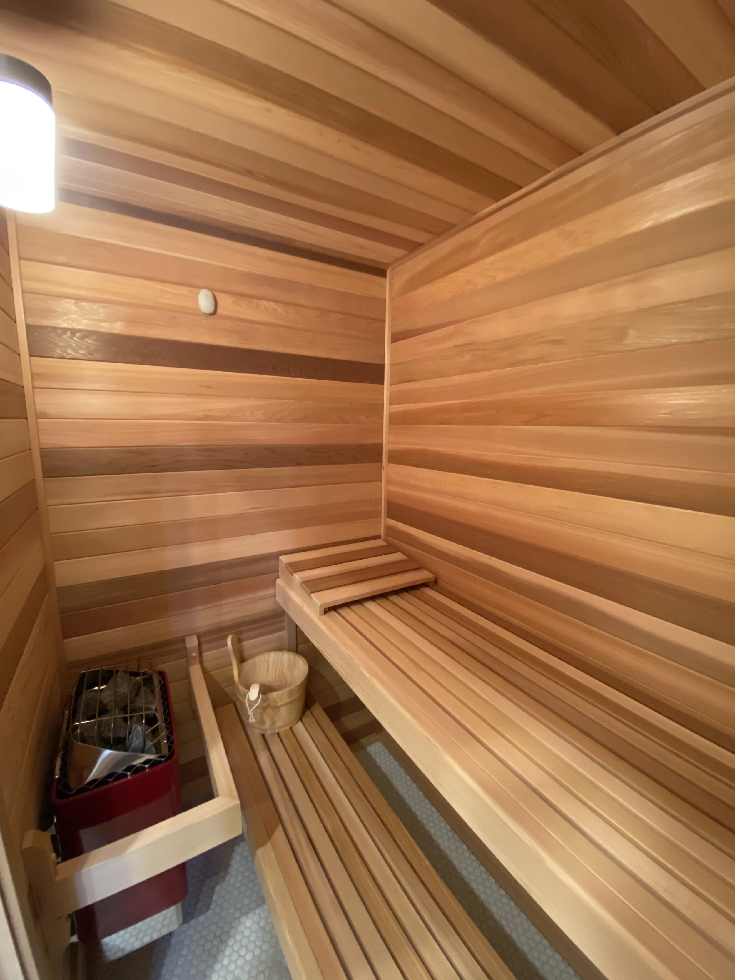 Wood-paneled sauna room with bench seating, a sauna heater, and a bucket with a ladle for water.