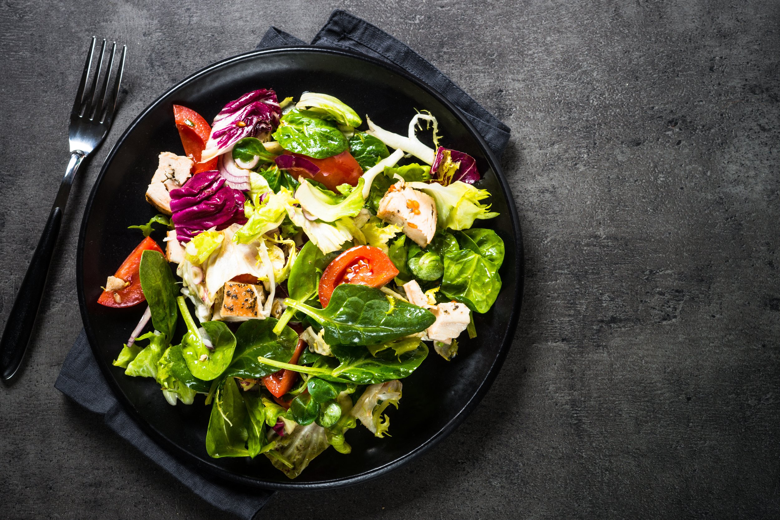 Green salad with chicken and vegetables on black.