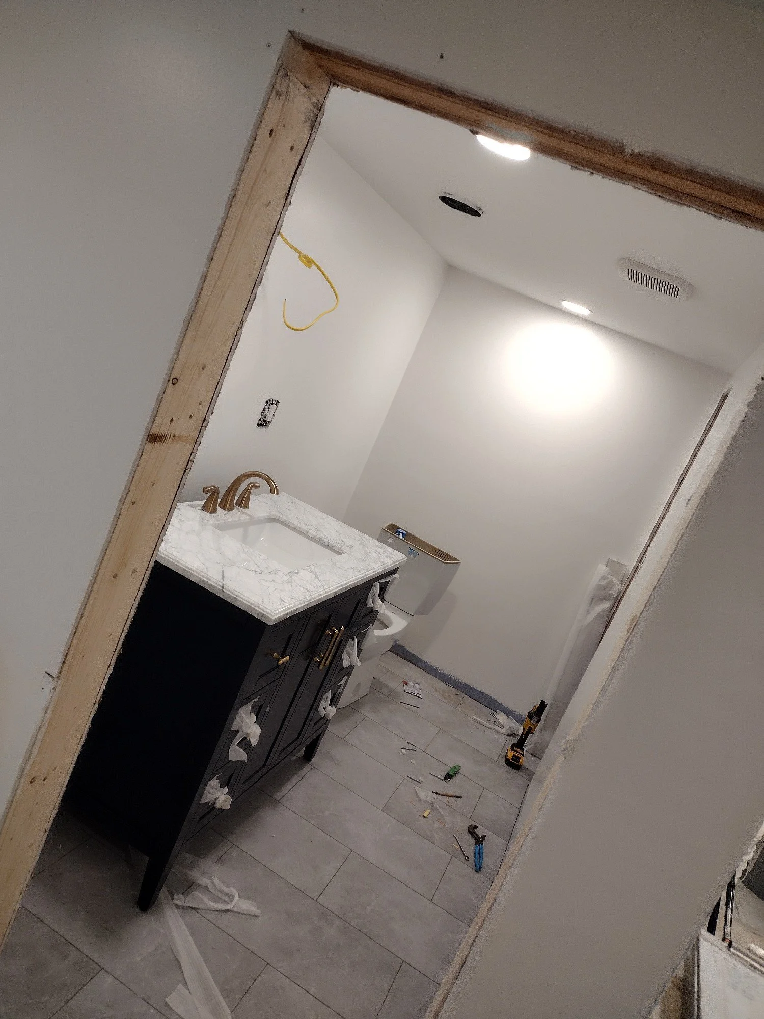 Bathroom under construction with white walls, a dark vanity with a marble countertop, a toilet, and construction tools scattered on the floor.