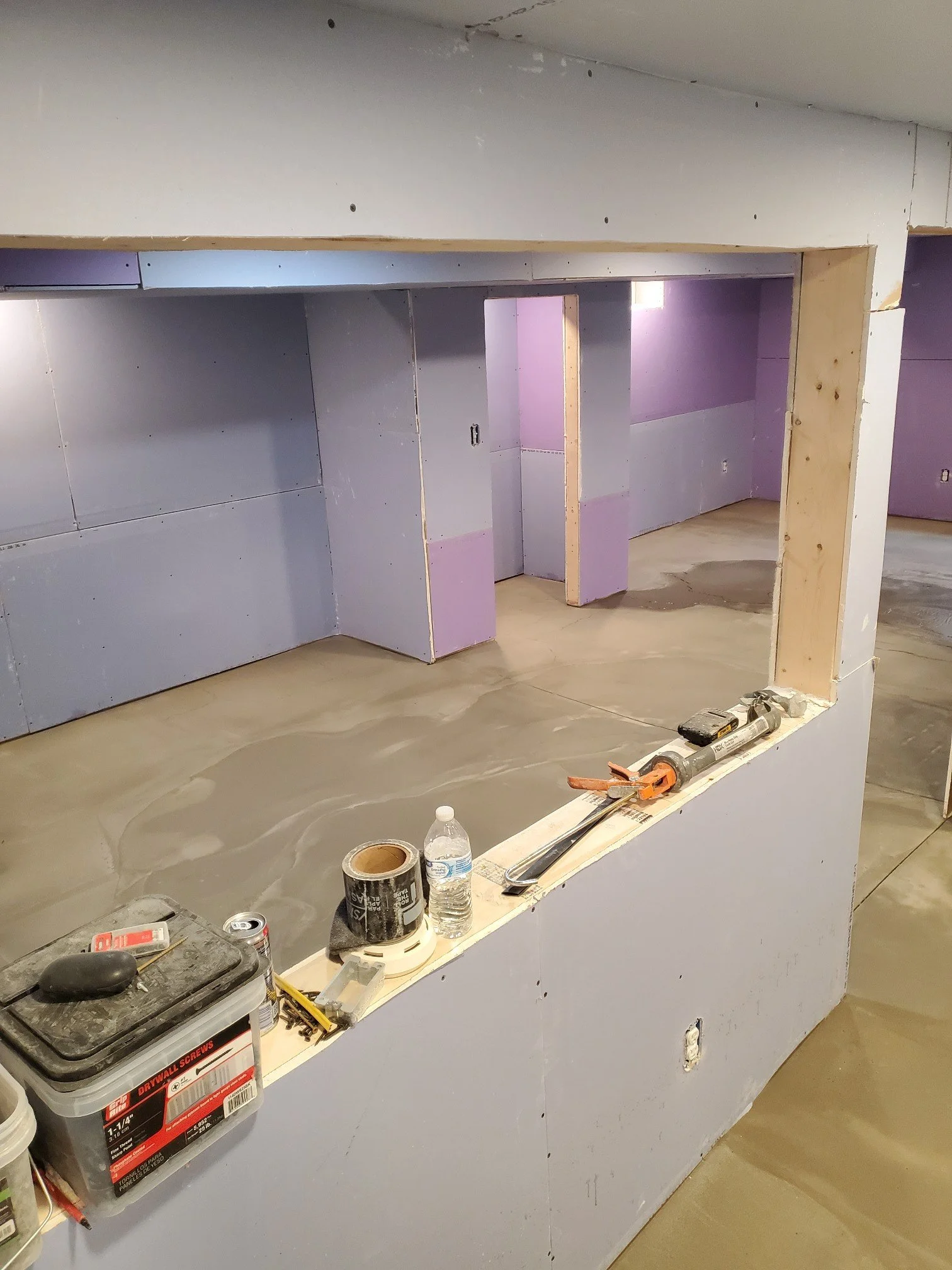 Interior of a construction site showing drywall installation with a partially built interior wall and construction tools on a ledge.