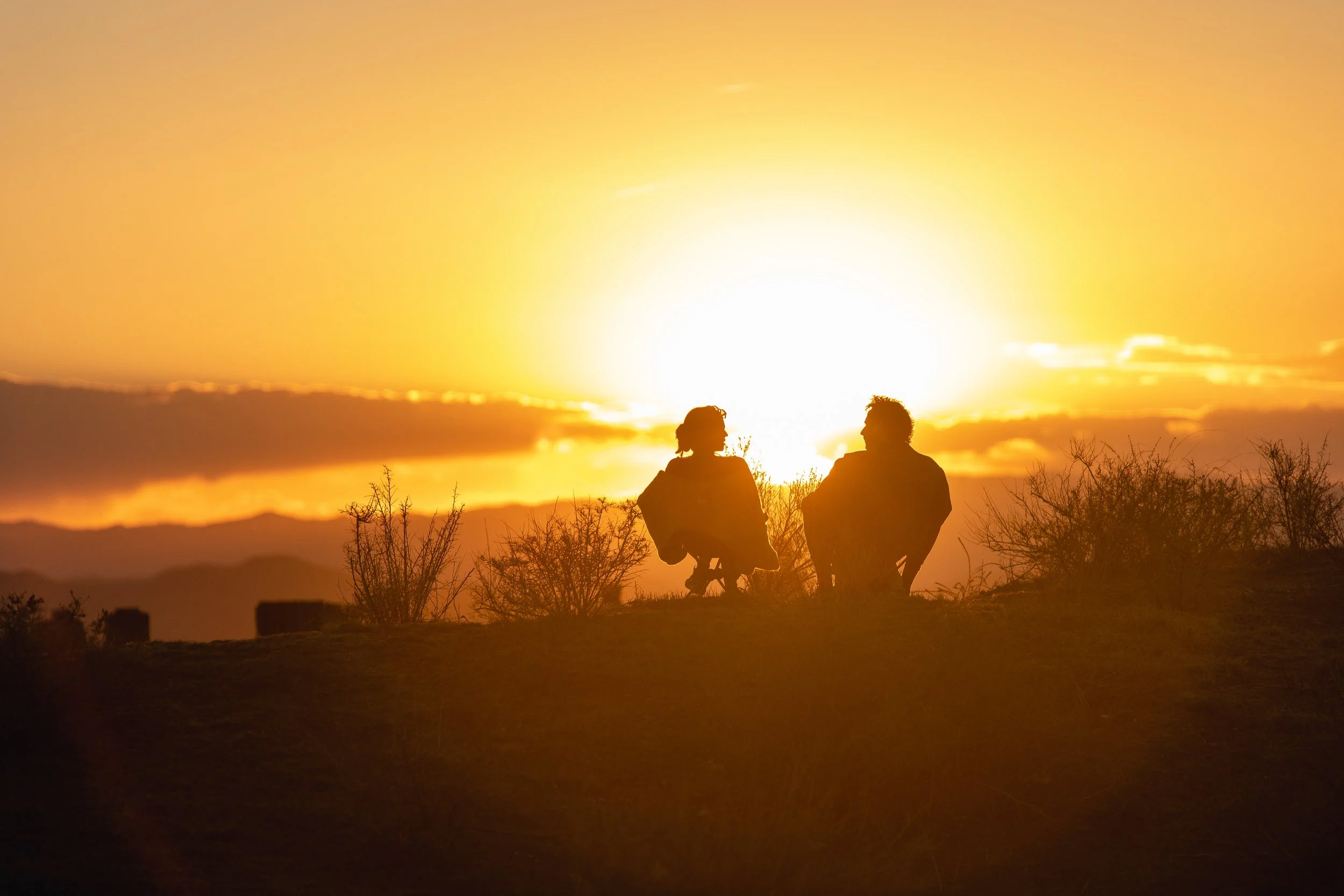 Sunset Silhouette of Couple sitting in chairs on mountaintop facing each other