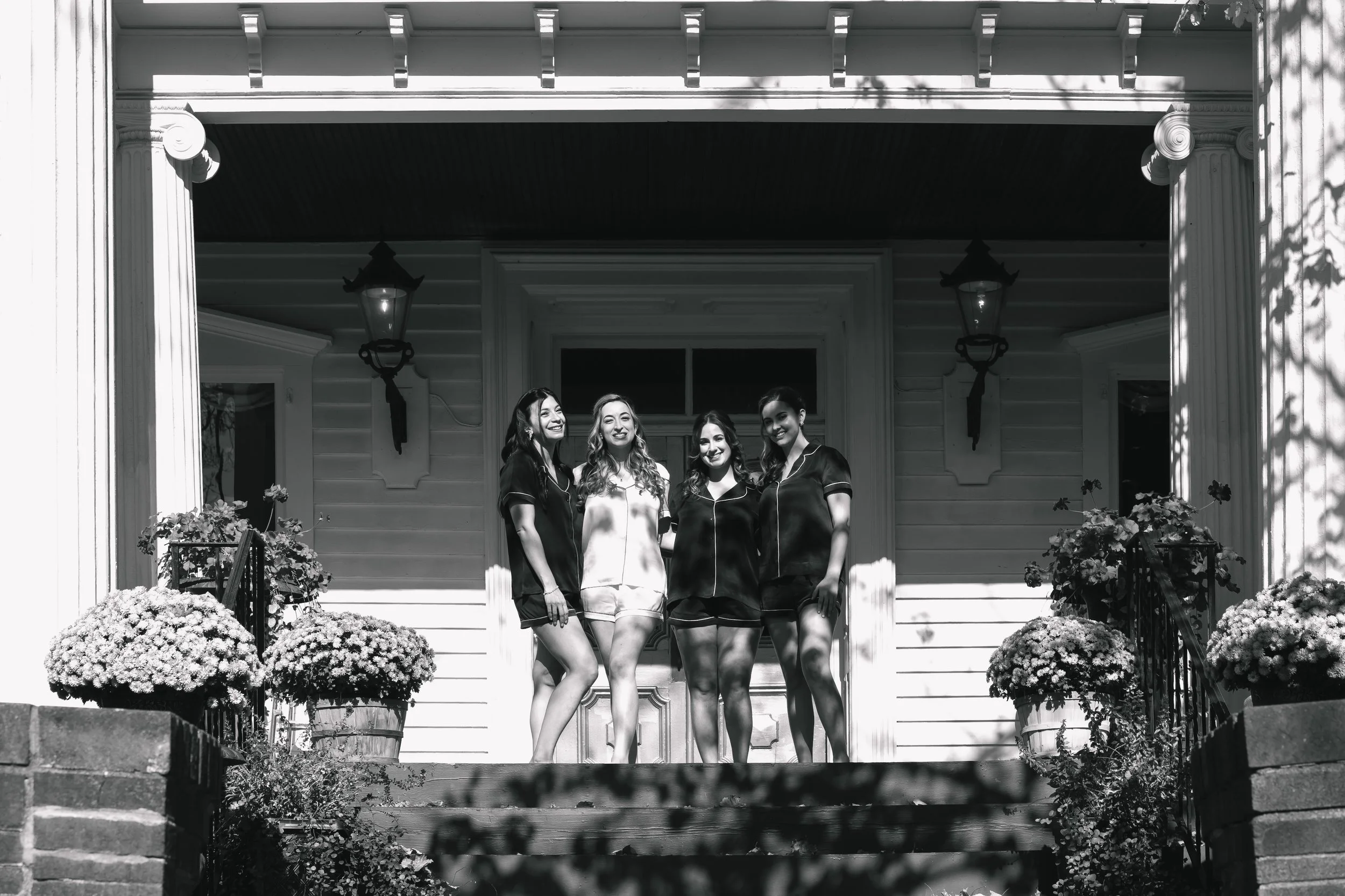 Bride and Bridesmaids smiling posing in pajamas on sunny porch of FEAST at Round Hill Wedding Venue