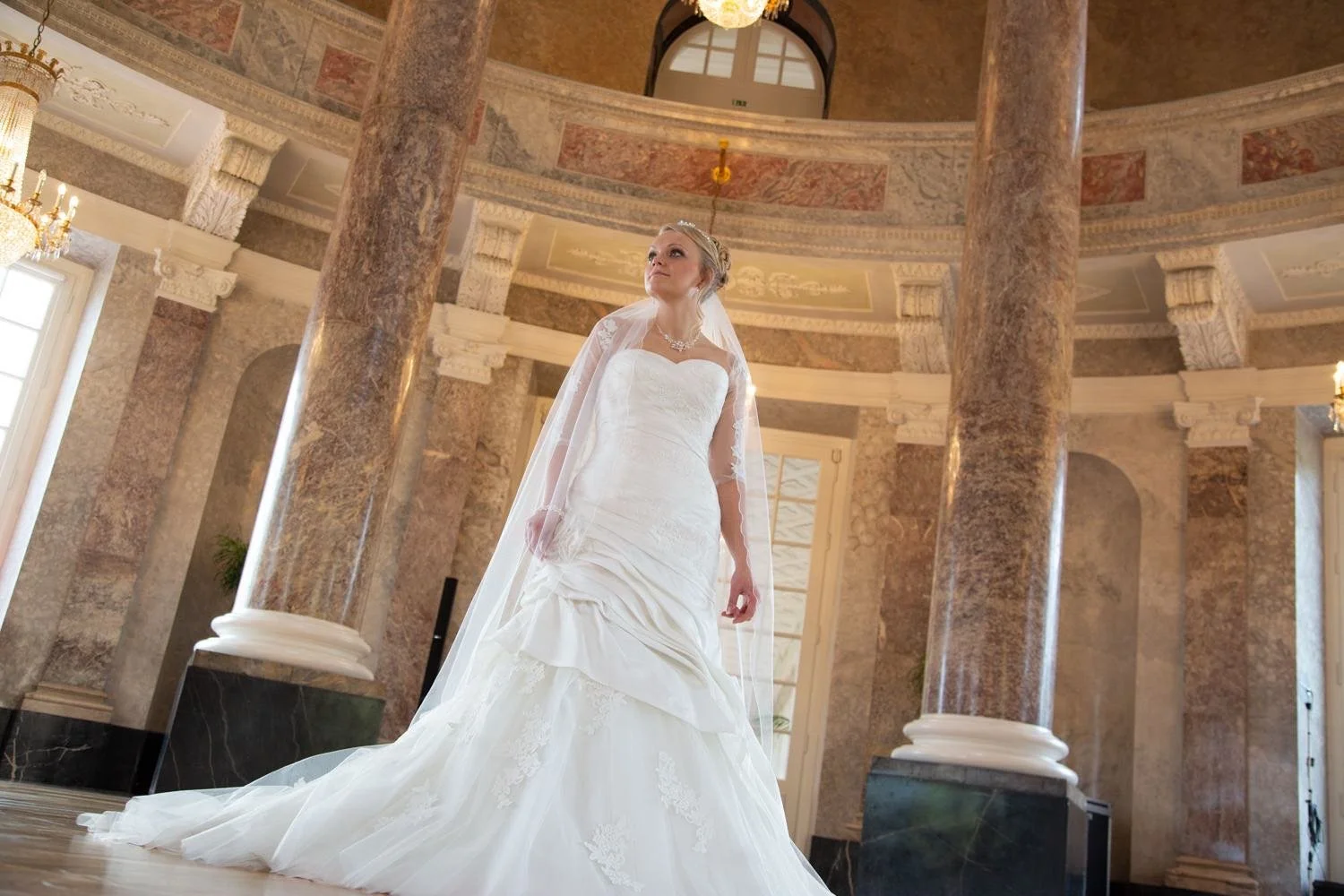 Braut in einer weißen Hochzeitskleid und Schleier steht in einem eleganten Saal in Darmstadt – von pixelfeder