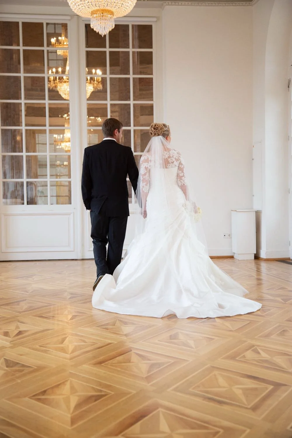 Ein Brautpaar geht in einem eleganten, hell erleuchteten Raum, mit kristallenen Kronleuchtern in Darmstadt – von pixelfeder