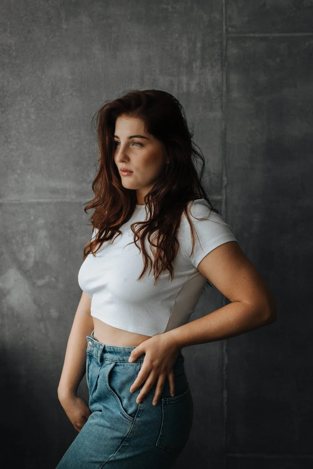 Portrait einer jungen Frau mit lockigen Haaren in einem Top und in Jeans vor einer Wand – von pixelfeder