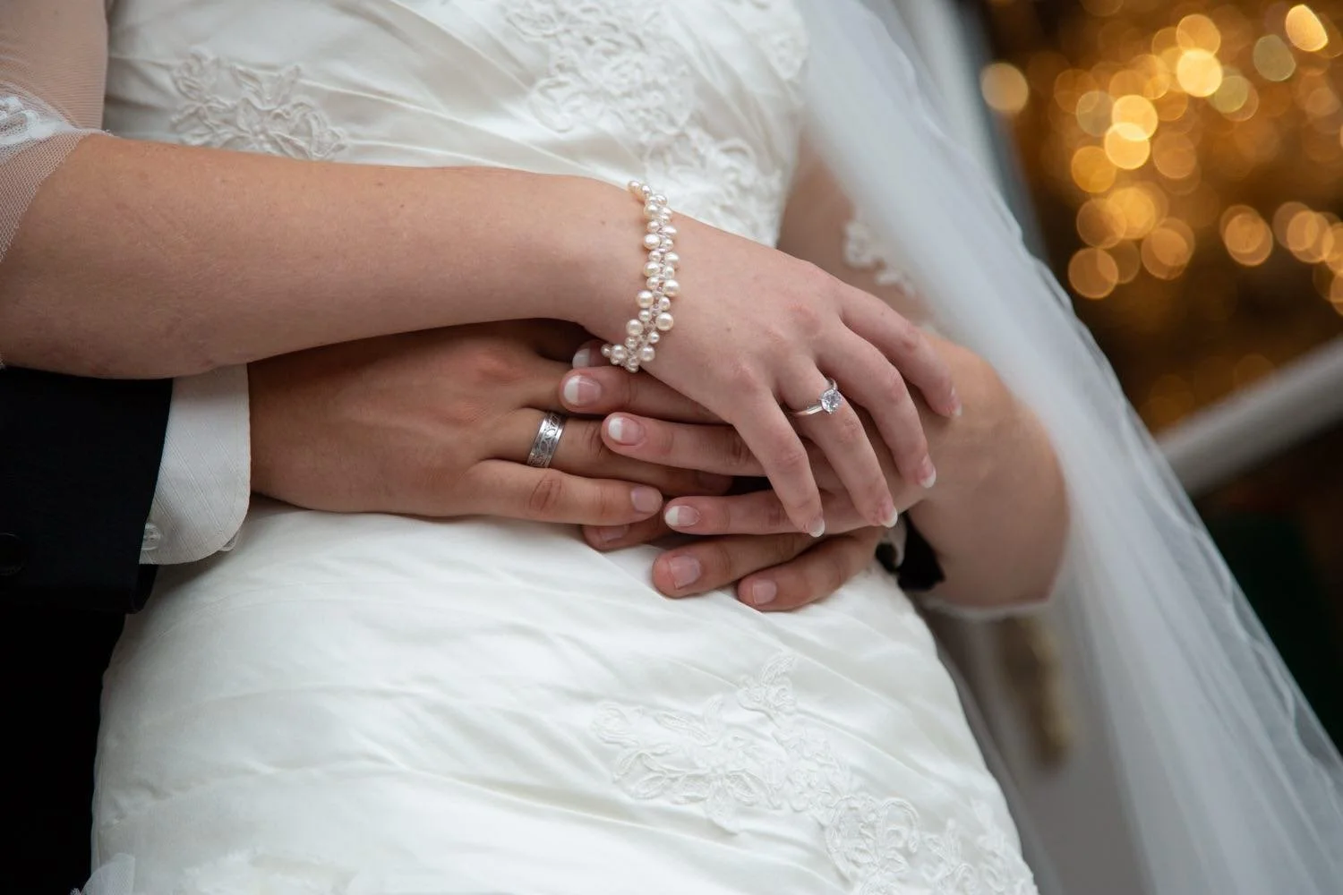 Nahaufnahme der Hände eines Brautpaares, mit Ringen und Perlenarmband auf einem weißen in Darmstadt – von pixelfeder